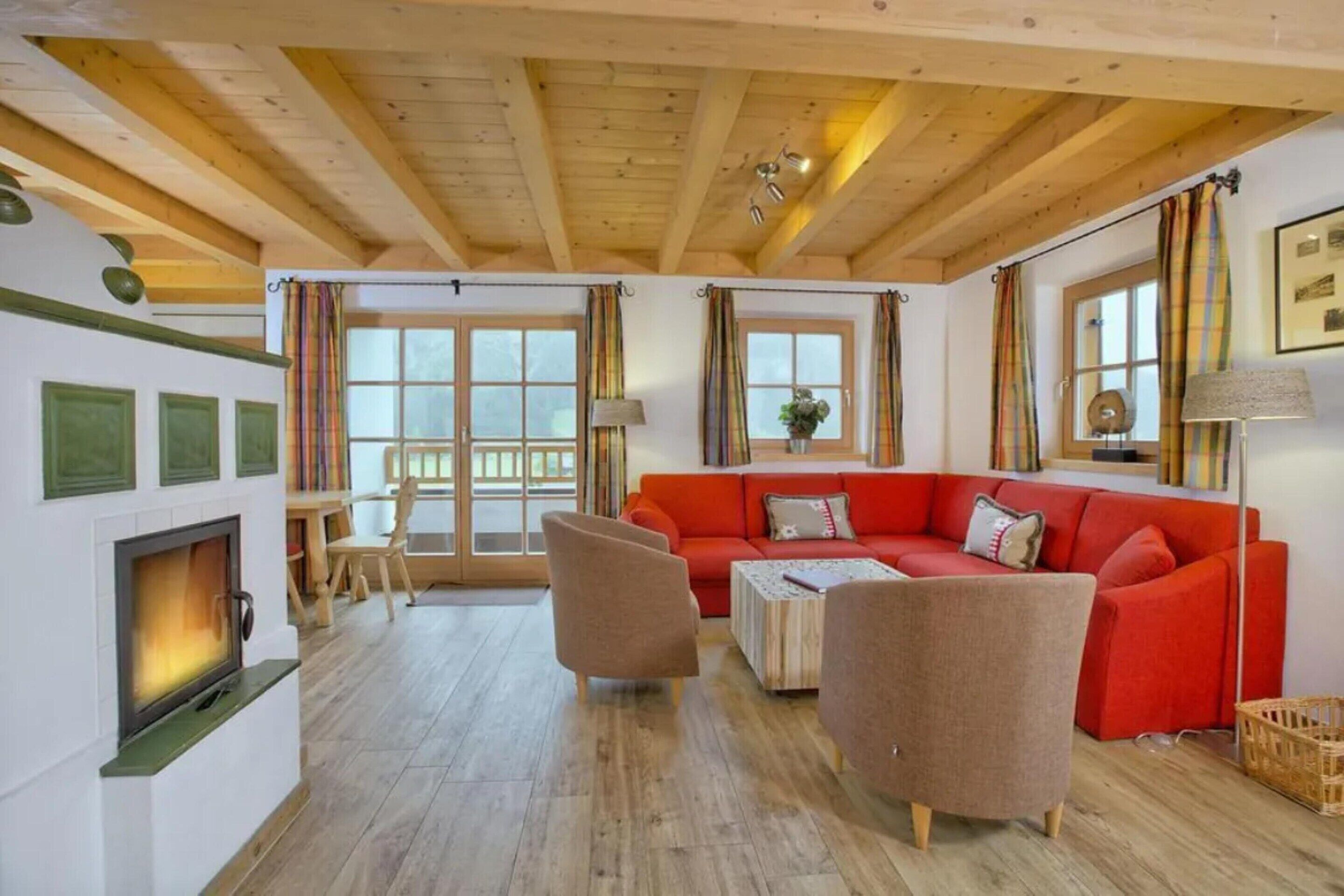 Een gezellige woonkamer met een open haard, een rode bank en een houten plafond.
