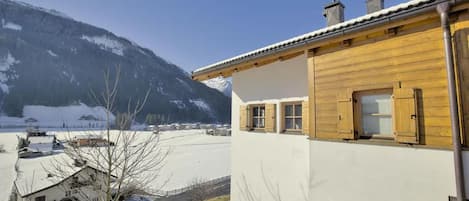 A wooden building with a white facade, a balcony, and a view of a snowy landscape with mountains in the background.