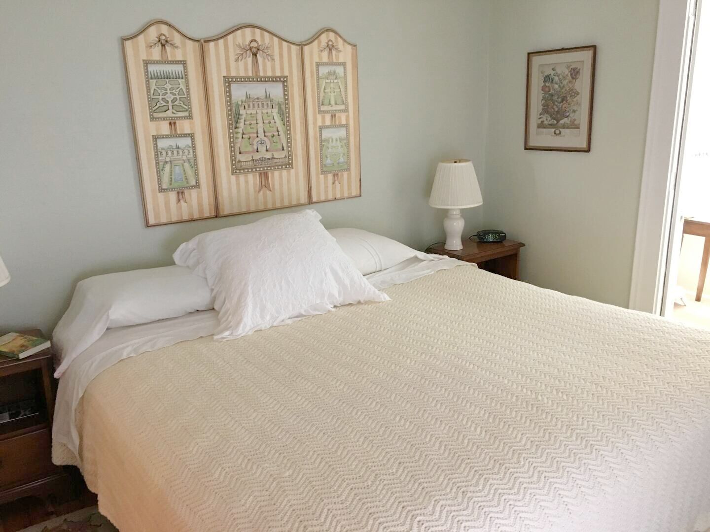 Un lit bien fait, avec du linge de lit blanc, une lampe de chevet et un panneau décoratif fixé au mur.