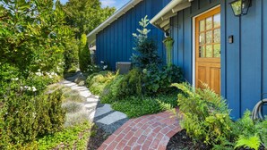 Une maison bleue avec un chemin de briques menant à une porte en bois, entourée d’une végétation luxuriante et d’un sentier de pierres.