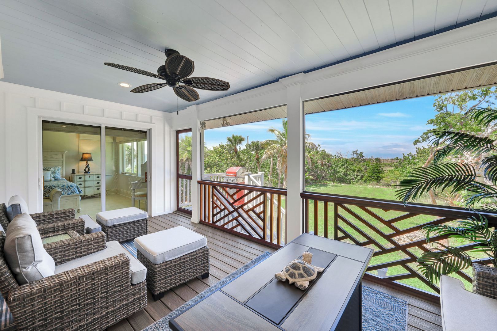 A covered outdoor area with wicker furniture, a ceiling fan, and a view of a lush landscape.