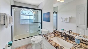 A modern bathroom with a glass-enclosed shower, a large vanity with a marble countertop, and a large mirror.