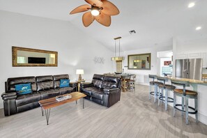 A modern living room with a sofa set, a coffee table, and a dining area with bar stools.