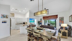 A spacious kitchen with white cabinets, a dining area with a large island, and a living room with a brown leather sofa.