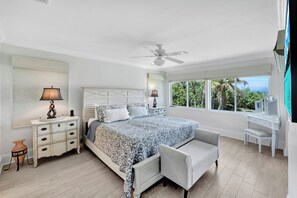 A bedroom with a bed, bedside tables, a desk, a chair, a ceiling fan, and a window with a view. - Rabbit road oasis just a short stroll to The Gulf! (Sanibel)