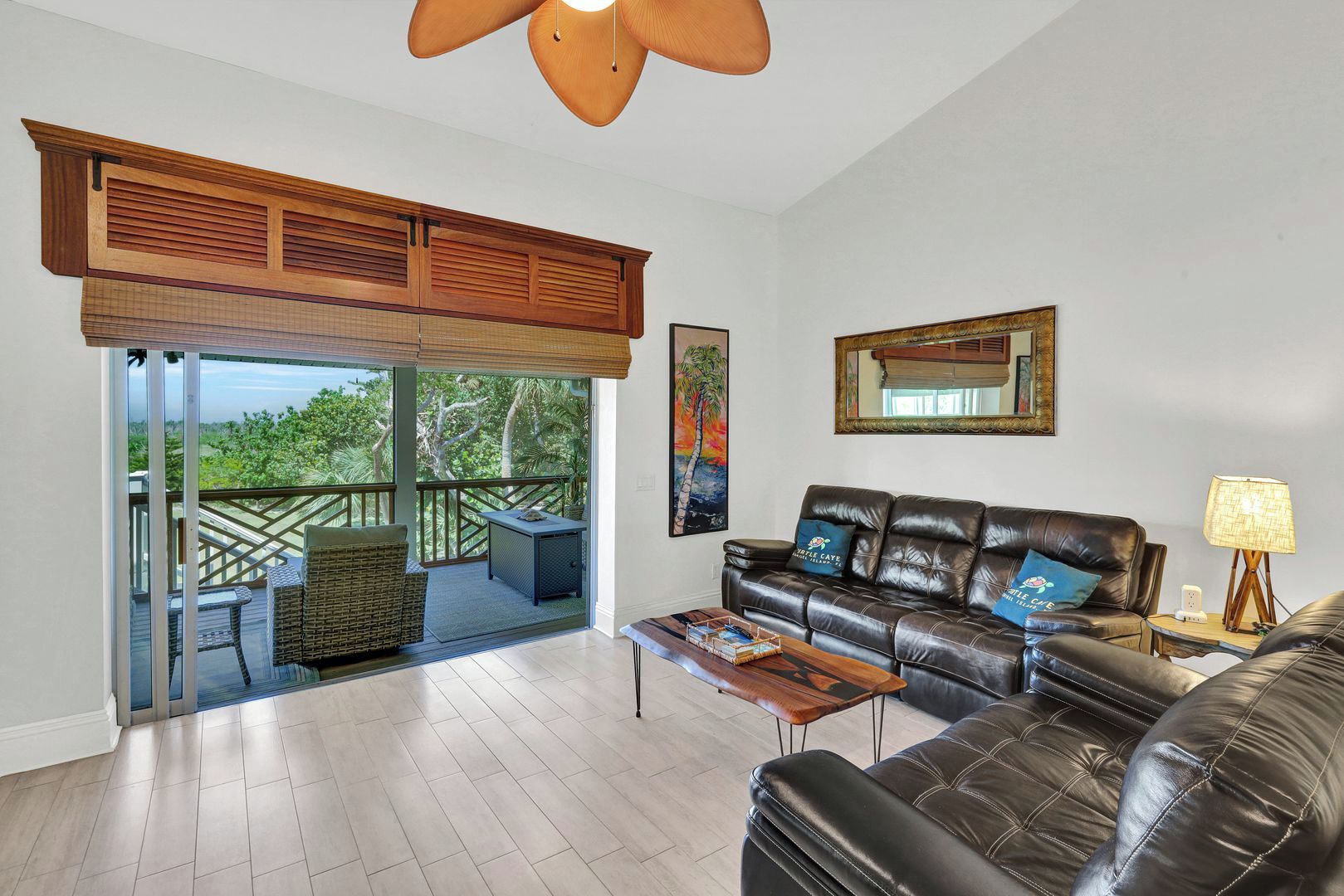 A spacious living room with a leather sofa, a coffee table, and a balcony with a view of greenery.