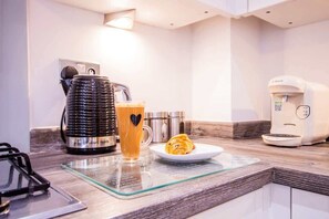 Una cocina con cafetera, taza de vidrio y plato con un pastel.