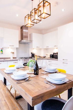 A modern kitchen with white cabinets, a wooden dining table set for six, and a hanging light fixture.