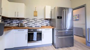 A modern kitchen with white cabinets, a stainless steel refrigerator, a built-in oven, and a tiled backsplash. - Cornwall House Home from Home Stay (Hartlepool)