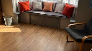 A room with a wooden floor, a window seat with cushions, a chair, and a trash bin. - Cornwall House Home from Home Stay (Hartlepool)