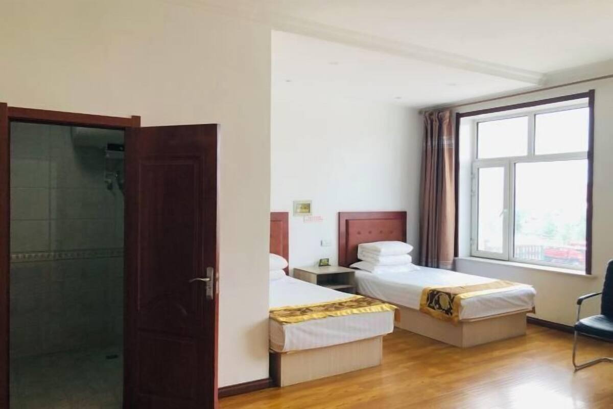 Une chambre d’hôtel avec deux lits, un plancher en bois, une grande fenêtre avec des rideaux et une chaise.