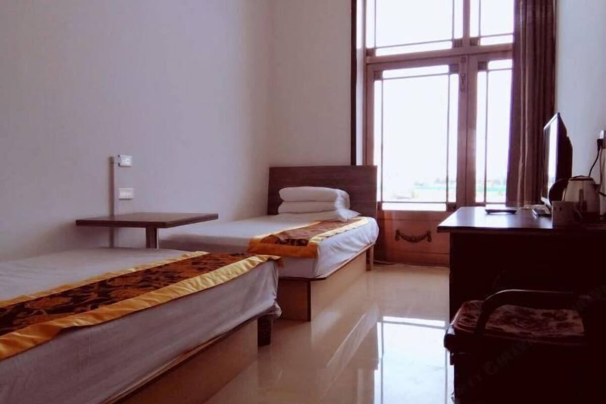 Une chambre d’hôtel avec deux lits, un bureau, une chaise et une fenêtre avec des rideaux.