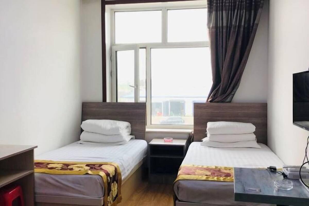 Une chambre d’hôtel avec deux lits simples, un bureau avec une chaise, une télévision et une fenêtre avec des rideaux.