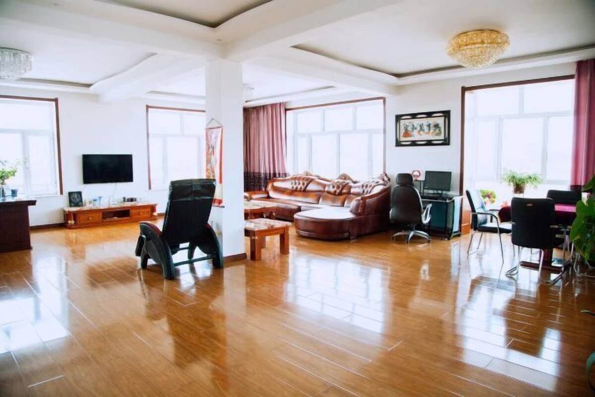 Un vaste espace de vie doté d’un plancher en bois, d’un canapé en cuir, d’une table basse, d’un téléviseur et d’un lustre.