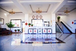 Vestíbulo de hotel con recepción, escalera y plantas en macetas.