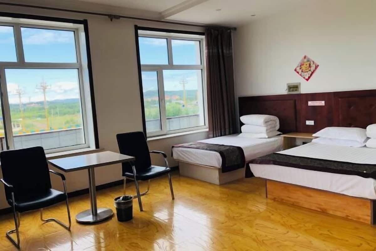Une chambre d’hôtel avec deux lits, un bureau et des chaises. De grandes fenêtres offrent une vue sur la verdure.