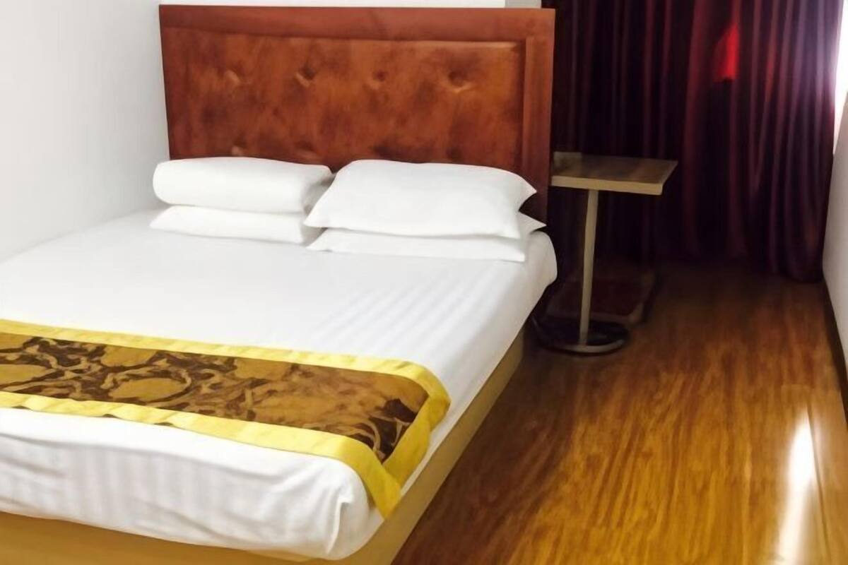 Un lit avec une tête de lit en bois, une literie blanche et un couvre-lit à motifs.