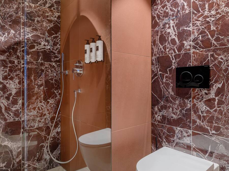 A modern bathroom with a glass-enclosed shower, a white toilet, and marble-patterned walls.