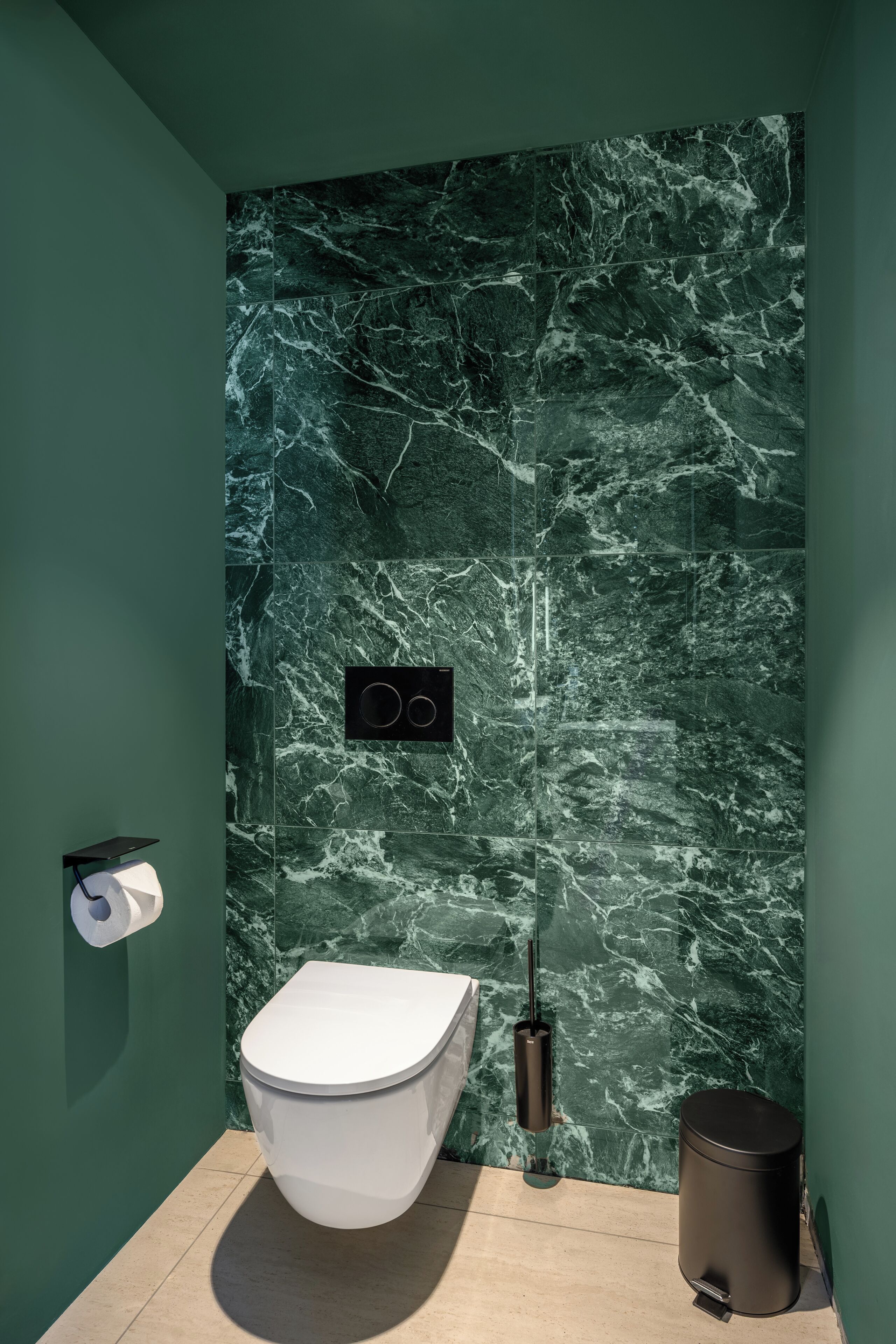 Un baño moderno con pared de mármol, un inodoro, un cesto de basura y un dispensador de toallas de papel.