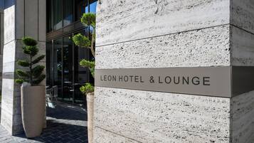 Das Leon Hotel & Lounge mit einer Steinfassade, einem großen Pflanzkübel mit kleinen Bäumen und freiem Blick auf den Eingang.