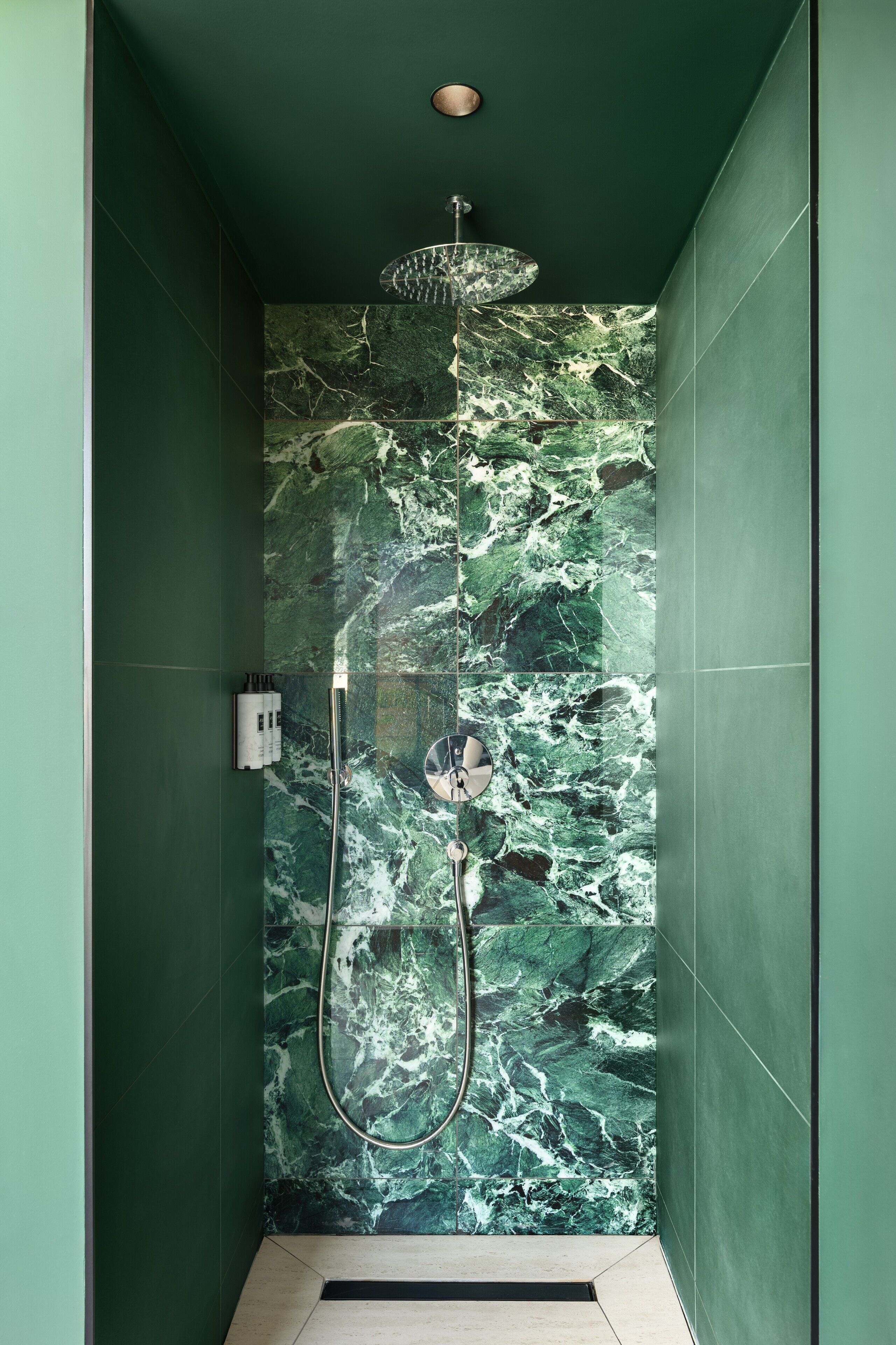 A shower with a marble wall and a handheld showerhead.