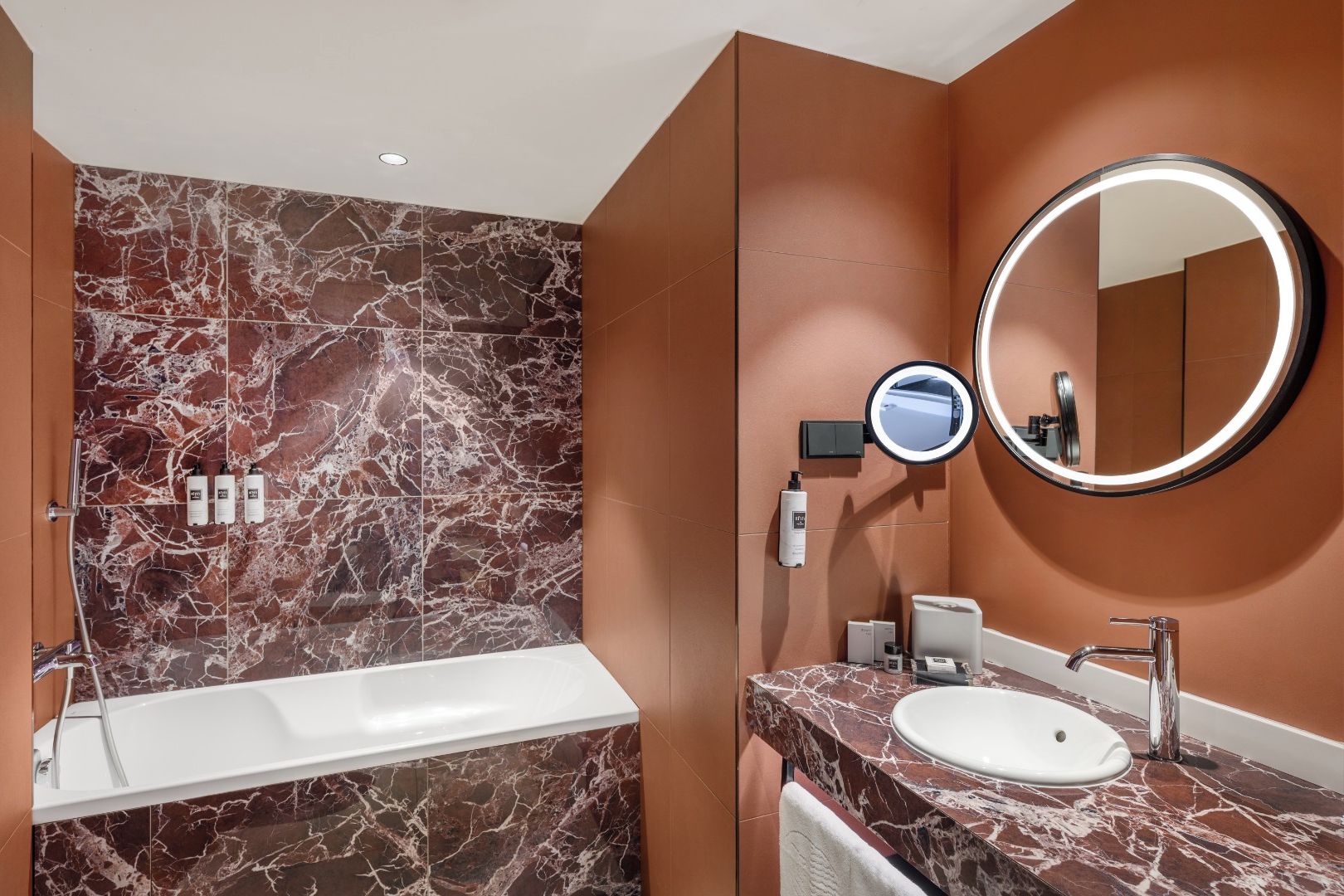 A modern bathroom with a marble vanity, a large mirror, and a handheld mirror.