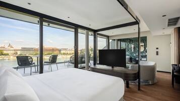 Habitación de hotel moderna con una cama grande, televisor y balcón con vistas a la ciudad.