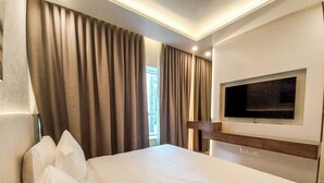 Habitación de hotel con una cama grande, un televisor de pantalla plana en la pared y una ventana con cortinas.