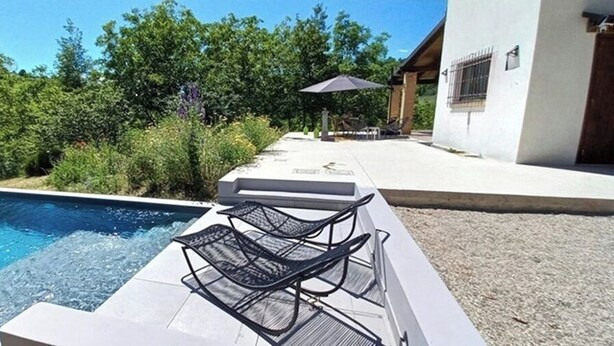 A swimming pool with lounge chairs, a patio area, and a view of greenery and a building in the background.