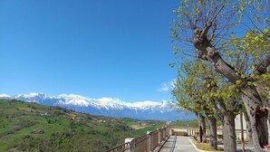 A pathway with a metal railing, leading to a scenic view of snow-capped mountains and green valleys.