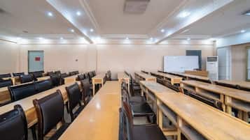 A conference room with rows of tables and chairs, a whiteboard, and a projector screen.