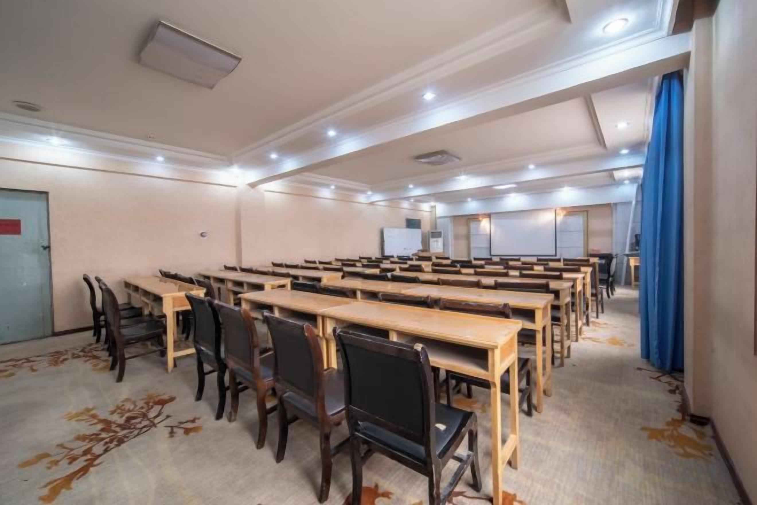 A conference room with rows of tables and chairs, a carpeted floor, and a door on the left.