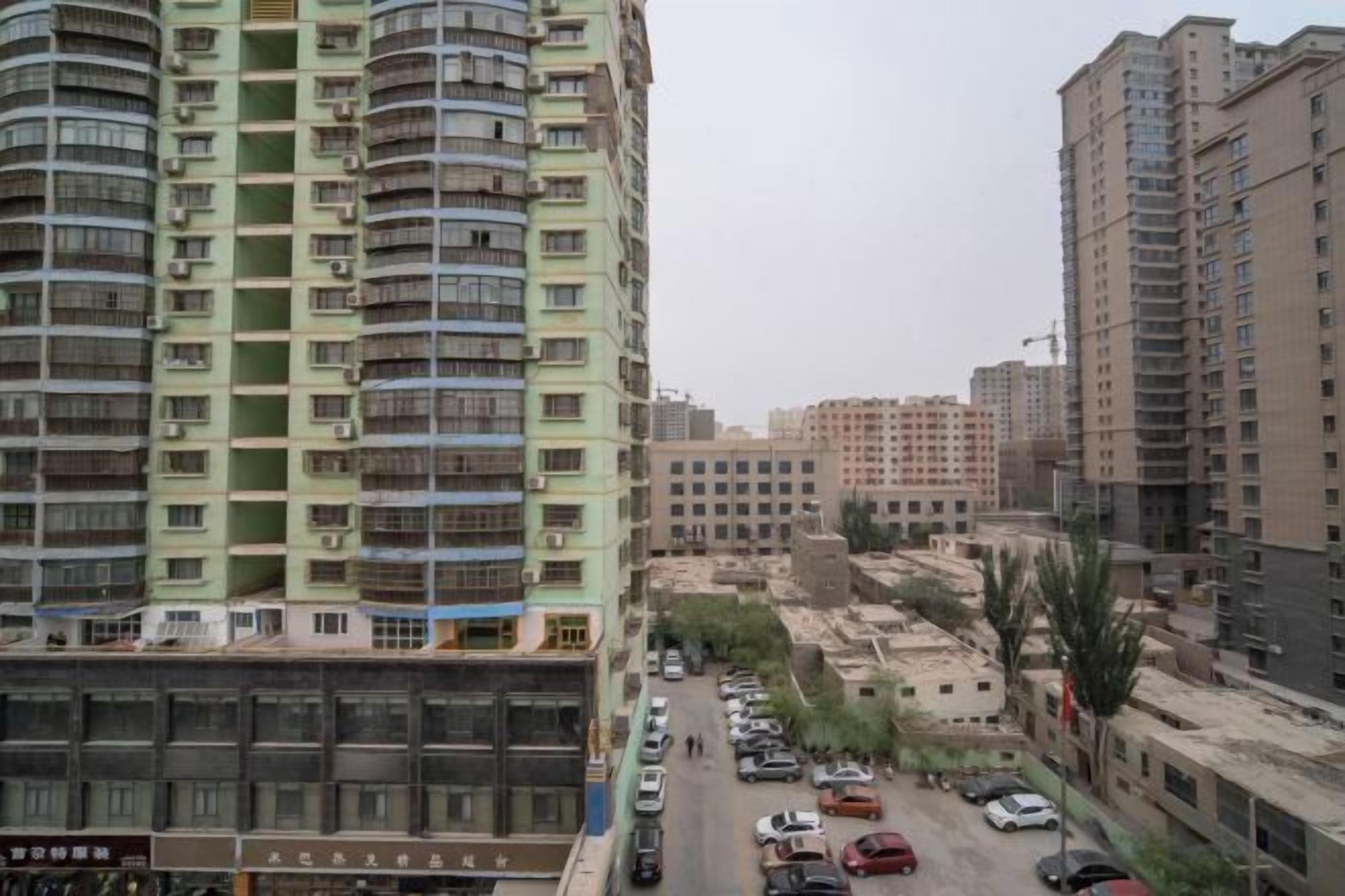 Un immeuble résidentiel à plusieurs étages, doté de balcons, avec un parking et un chantier de construction en arrière-plan.