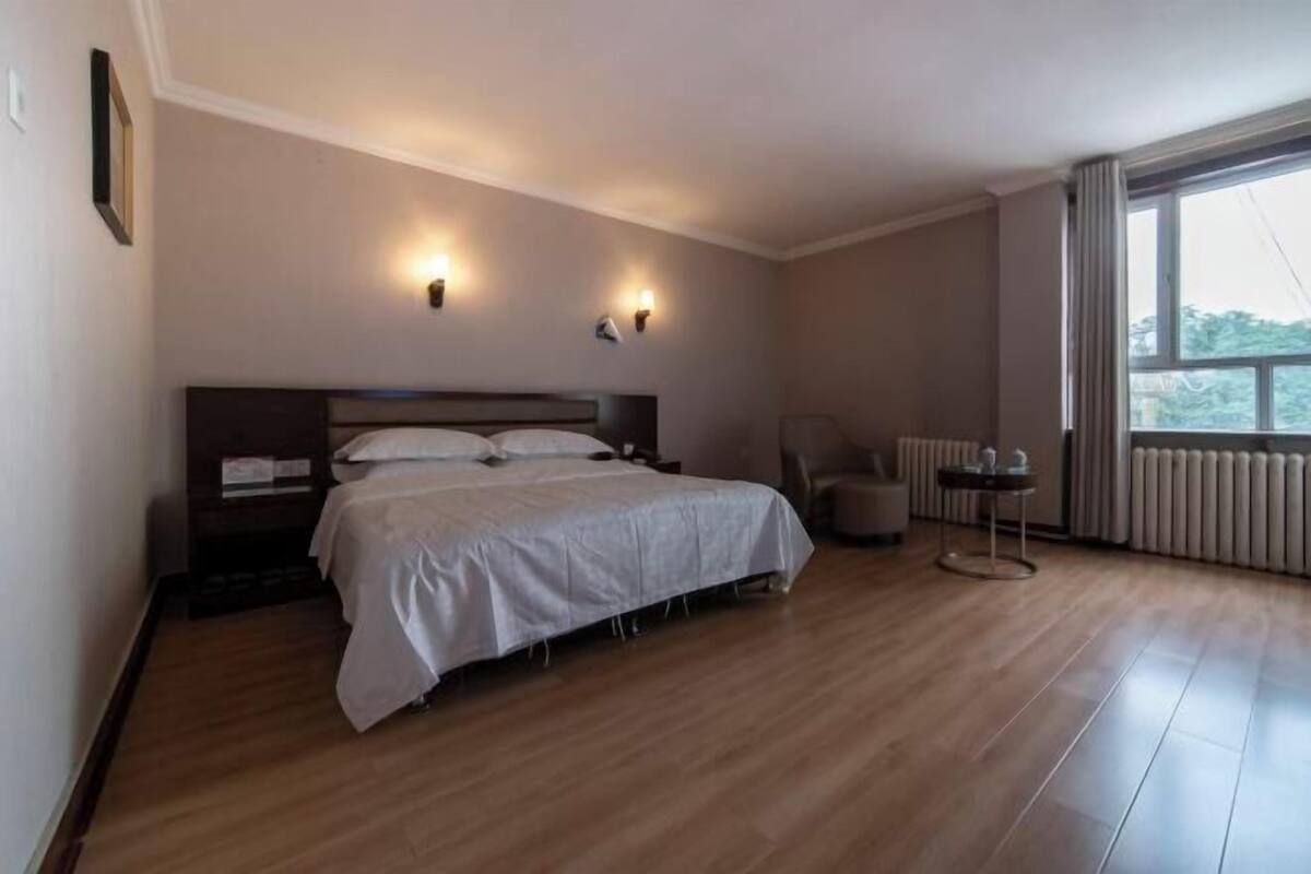 A hotel room with a bed, a chair, a small table, and a window.