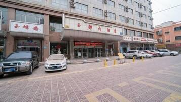 A multi-story building with a storefront on the ground floor, several parked cars, and a patterned pavement.