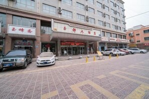 A multi-story building with a storefront on the ground floor, several parked cars, and a patterned pavement. - Yudu Hotel (Hotan City)