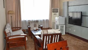 A room with a wooden dining table, chairs, a sofa, a TV, and a window with curtains. - Yudu Hotel (Hotan City)