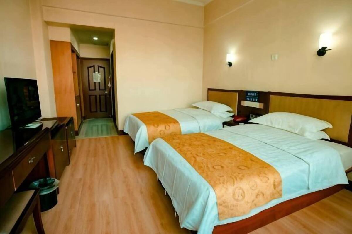Ein Hotelzimmer mit zwei Betten, einem Fernseher, einem Schreibtisch und einer Tür zu einem anderen Raum.