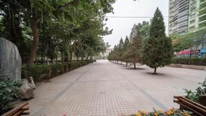 A paved walkway lined with trees and planters with flowers. - Yudu Hotel (Hotan City)