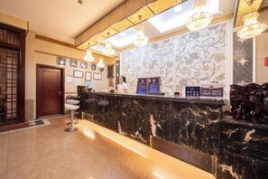 A hotel reception area with a marble counter, framed pictures on the wall, and a reception desk. - Yudu Hotel (Hotan City)