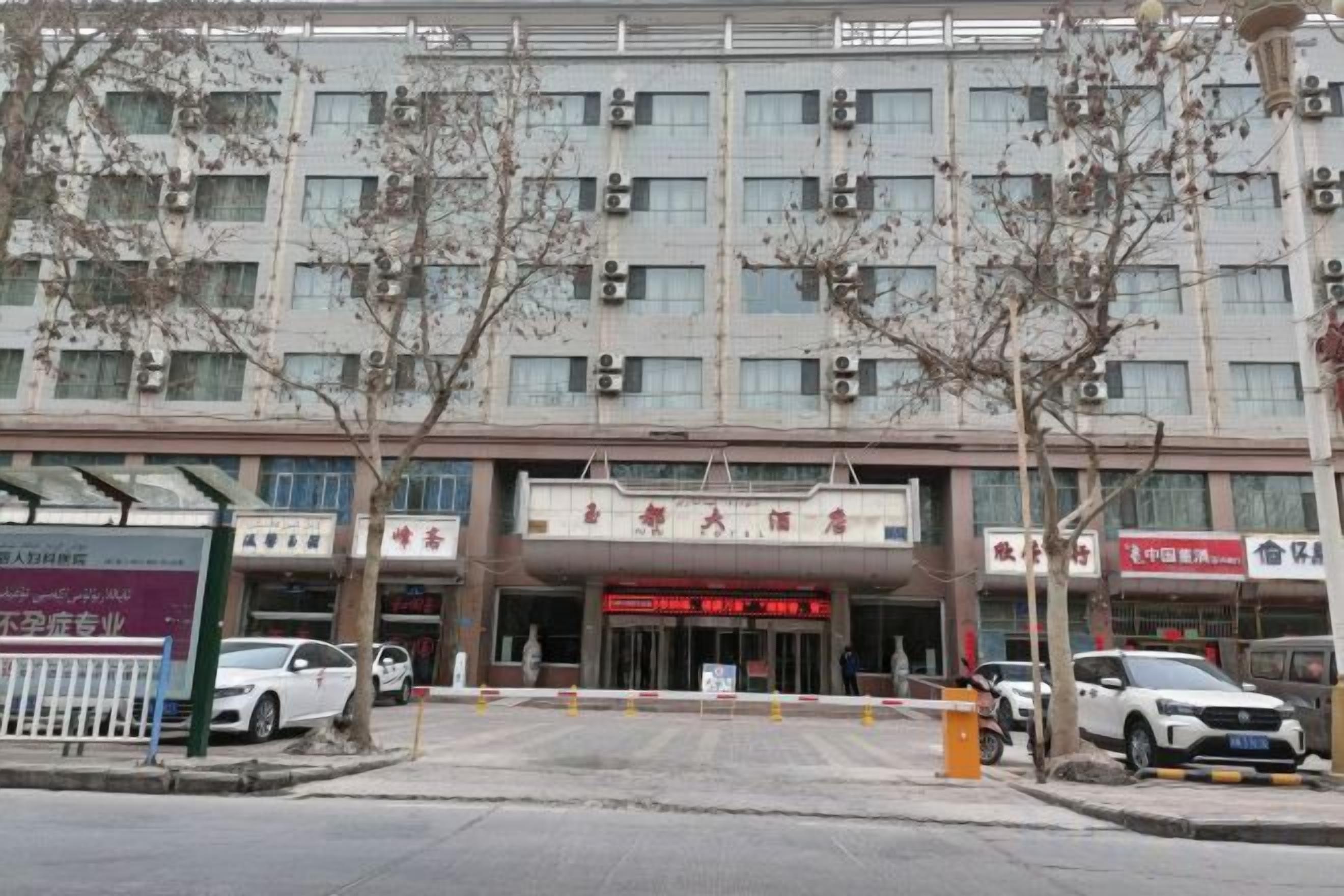 A multi-story building with a central entrance, surrounded by parked cars and trees.