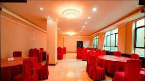 A conference room with round tables and red chairs, large windows, and a chandelier. - Yudu Hotel (Hotan City)