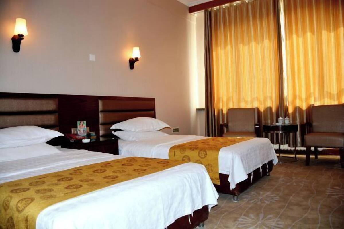 A hotel room with two beds, a small table, a chair, and a window with curtains.