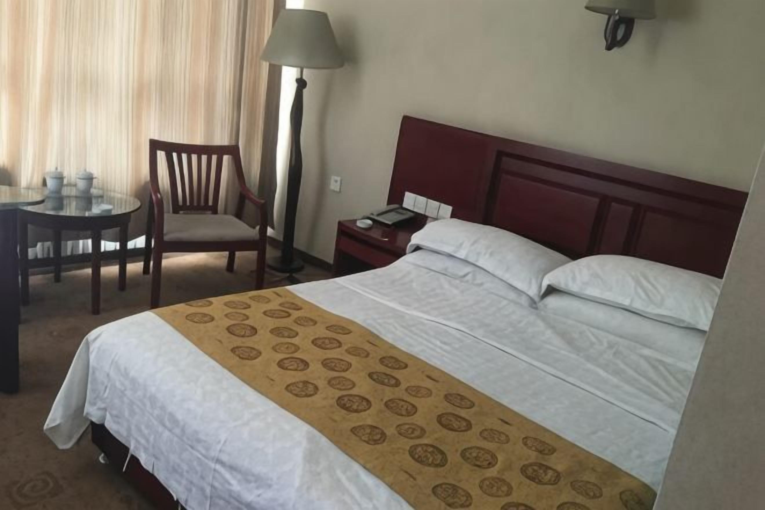 Una habitación de hotel con una cama, un escritorio con silla, una lámpara y una mesita de noche.