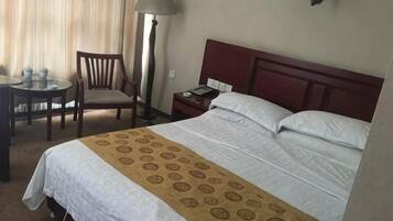Una habitación de hotel con una cama, un escritorio con silla, una lámpara y una mesita de noche.