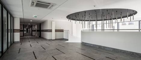 A modern hotel lobby with a long corridor, a reception desk, and a large window.