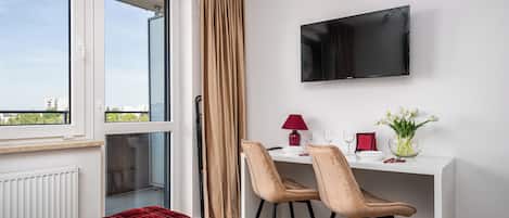 A hotel room with a bed, a desk with two chairs, a TV, a clock, and a window with curtains.