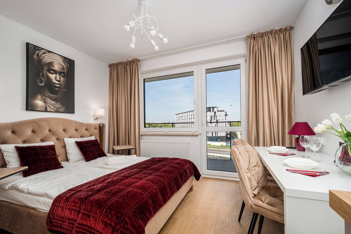 A hotel room with a large bed, a desk with a chair, a TV, and a window with curtains.