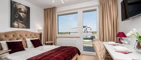 Ein Hotelzimmer mit einem großen Bett, einem Schreibtisch mit Stuhl, einem Fernseher und einem Fenster mit Vorhängen.