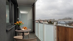 A balcony with a table, chairs, a vase of flowers, and a croissant. - Pileckiego Residence (Warsaw)